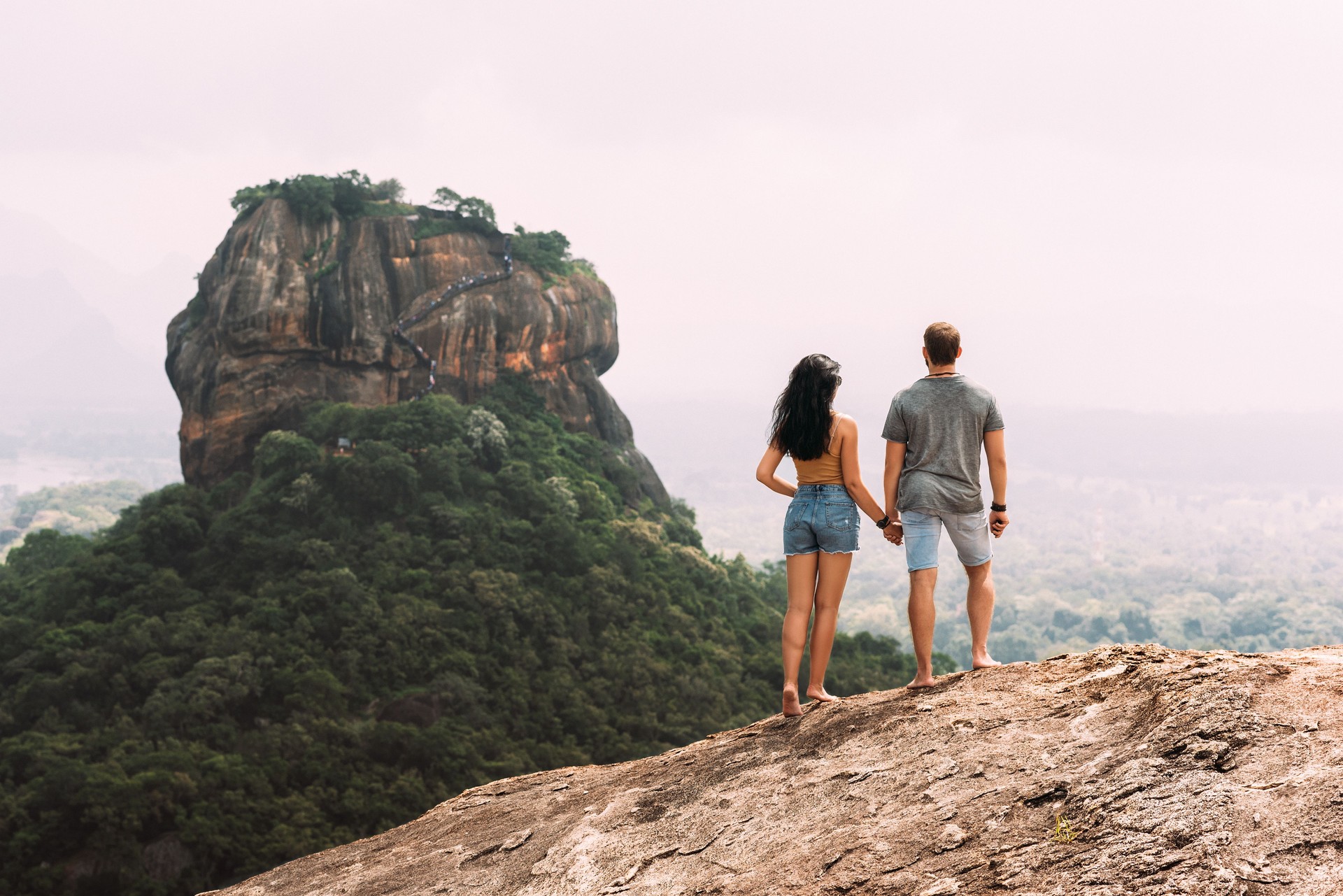 A couple in love on a rock admires the beautiful views. Boy and girl on the rock. A couple in love travels. Couple in Sri Lanka. Honeymoon in Asia. Man and woman in Sigiriya. Rear view pair